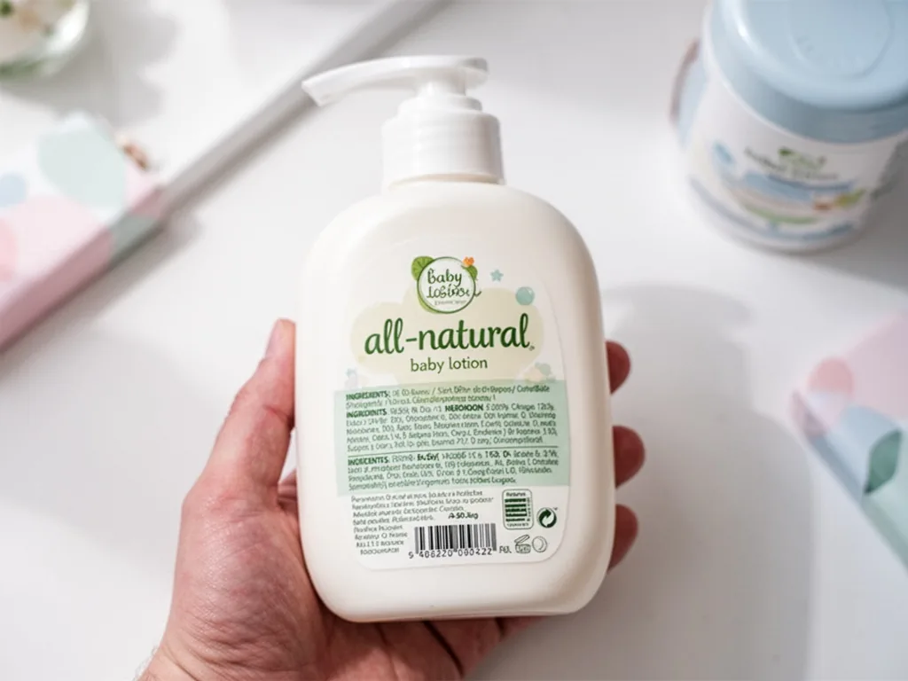 A close-up of a baby lotion bottle with a large 'all-natural' label on the front and tiny ingredients on the back, held